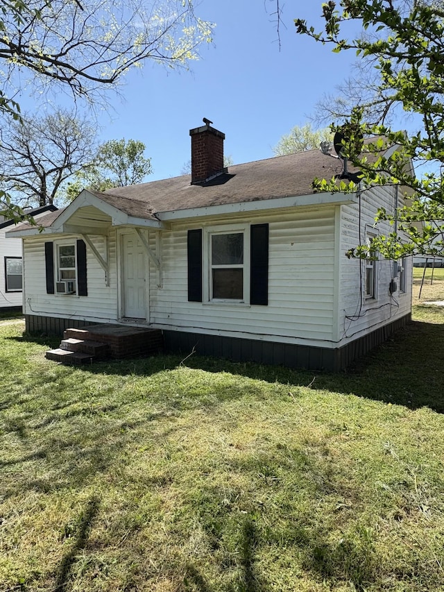view of front facade with a front yard, a chimney, and a shingled roof
