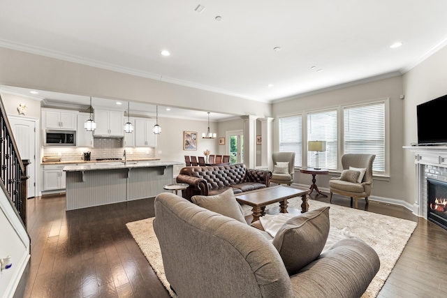 living area with a healthy amount of sunlight, a tiled fireplace, decorative columns, and dark wood finished floors