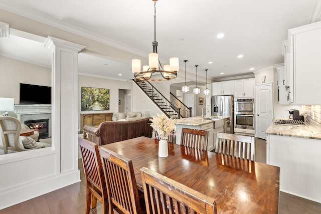 dining room featuring an inviting chandelier, ornamental molding, a fireplace, recessed lighting, and dark wood-type flooring