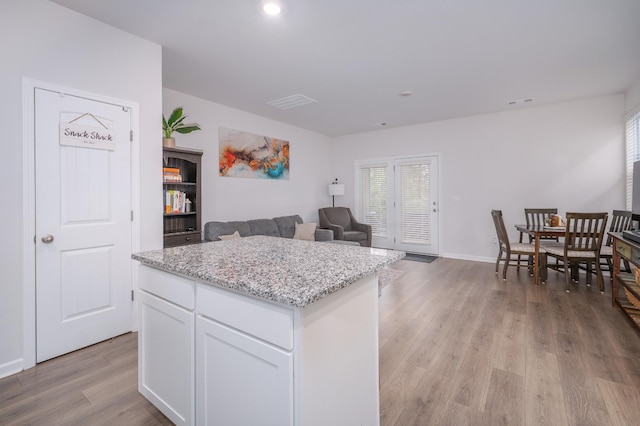 kitchen featuring white cabinetry, a kitchen island, light stone counters, open floor plan, and light wood finished floors