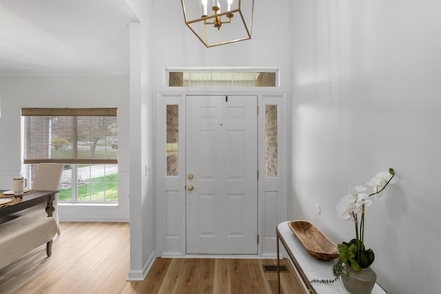 foyer entrance with crown molding, an inviting chandelier, light wood-style flooring, visible vents, and baseboards