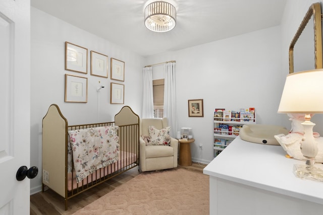 bedroom with a crib, baseboards, and wood finished floors
