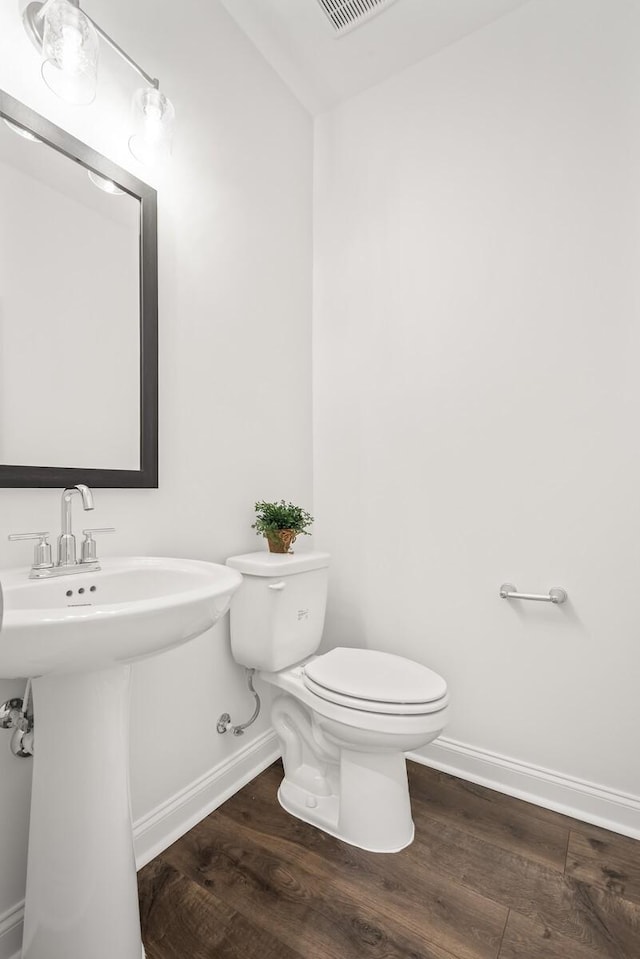 half bath with wood finished floors, baseboards, and toilet