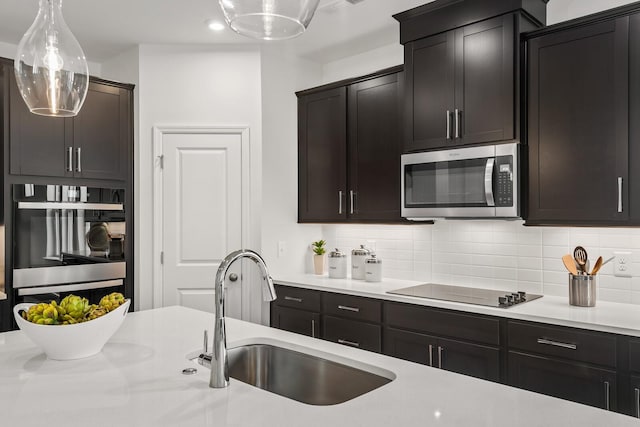 kitchen with a sink, decorative backsplash, black electric cooktop, light countertops, and stainless steel microwave