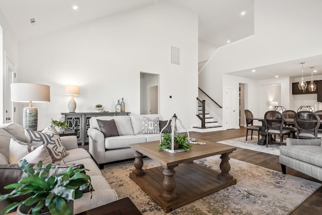 living area with stairway, wood finished floors, visible vents, and high vaulted ceiling