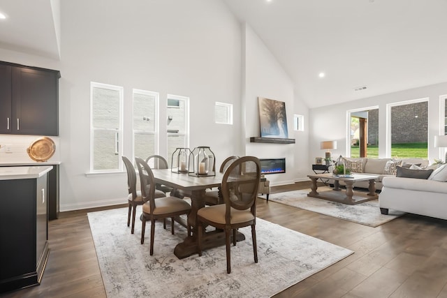 dining room featuring baseboards, a glass covered fireplace, high vaulted ceiling, and dark wood-type flooring