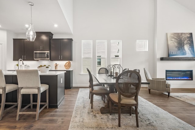 dining space featuring wood finished floors, a glass covered fireplace, baseboards, a high ceiling, and recessed lighting