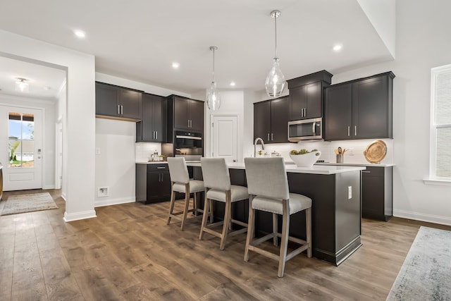 kitchen featuring tasteful backsplash, wood finished floors, stainless steel appliances, light countertops, and baseboards