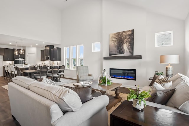 living room with baseboards, a glass covered fireplace, high vaulted ceiling, and dark wood-style flooring