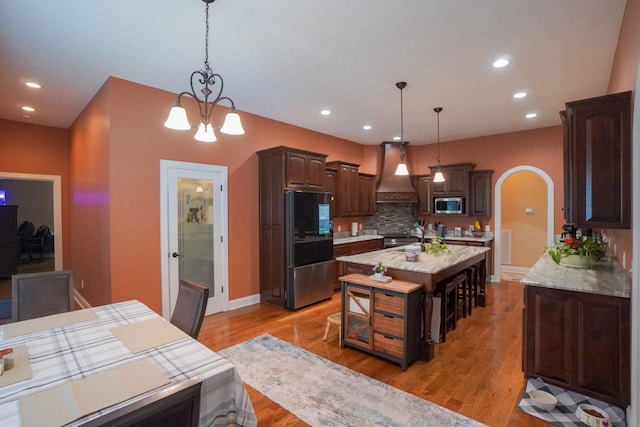 kitchen featuring tasteful backsplash, stainless steel appliances, dark brown cabinets, arched walkways, and custom exhaust hood