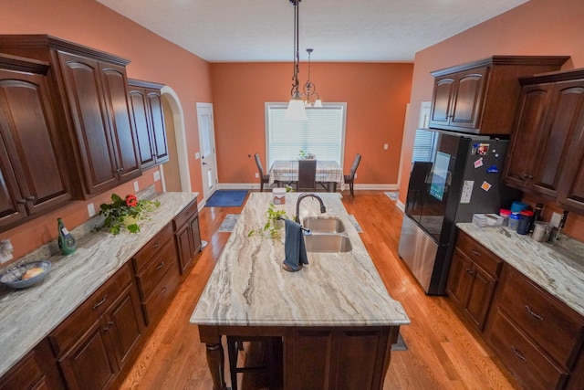 kitchen featuring freestanding refrigerator, a kitchen island with sink, light wood-style flooring, and a sink