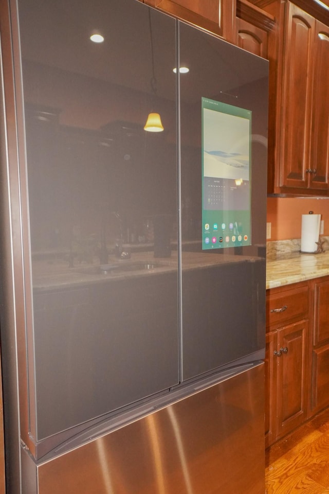 interior details featuring light stone countertops, decorative light fixtures, light wood-style floors, brown cabinets, and refrigerator with glass door