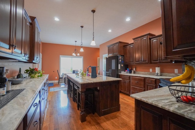 kitchen with light stone counters, a breakfast bar area, freestanding refrigerator, a kitchen island, and light wood-type flooring