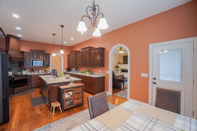 kitchen featuring an inviting chandelier, premium range hood, arched walkways, appliances with stainless steel finishes, and wood finished floors