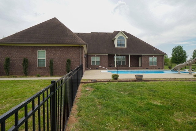 back of house featuring fence, a yard, brick siding, and a fenced in pool