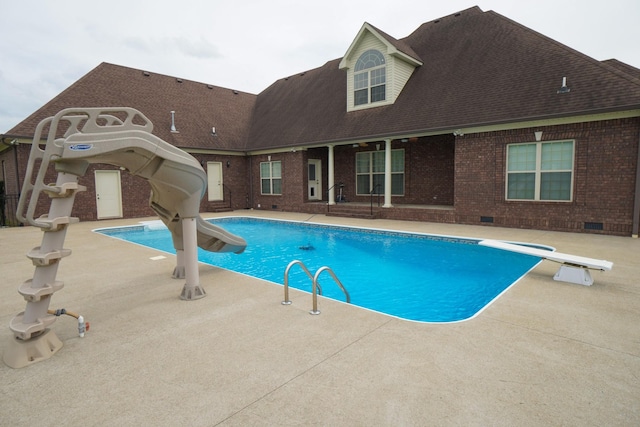 outdoor pool featuring a water slide, a diving board, and a patio area