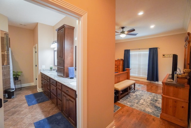 full bath featuring double vanity, ornamental molding, ceiling fan, a sink, and baseboards