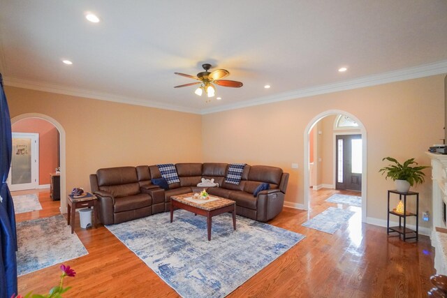 living area featuring arched walkways, a ceiling fan, and crown molding