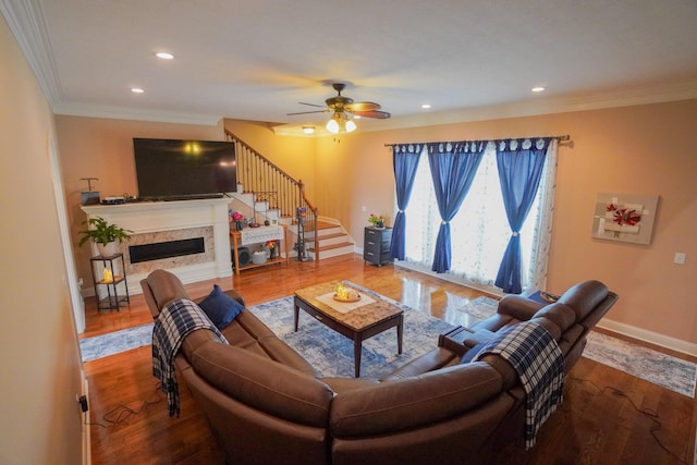 living area featuring wood finished floors, stairs, ceiling fan, a premium fireplace, and crown molding