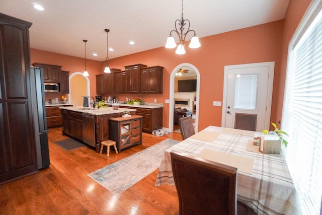 kitchen featuring arched walkways, a kitchen island with sink, light countertops, and stainless steel appliances