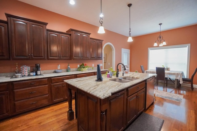 kitchen featuring arched walkways, hanging light fixtures, light wood-style flooring, dishwasher, and a sink