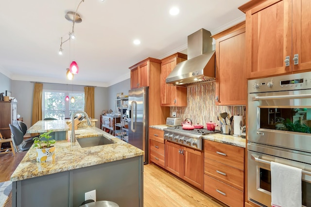 kitchen with wall chimney range hood, crown molding, light wood-style floors, appliances with stainless steel finishes, and a sink