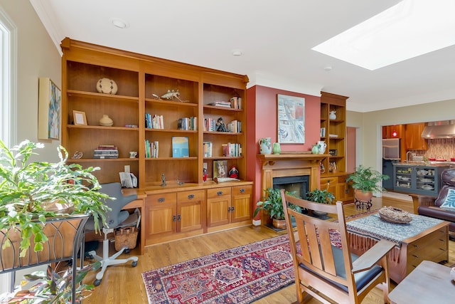 dining room featuring a fireplace, light wood finished floors, crown molding, and a skylight