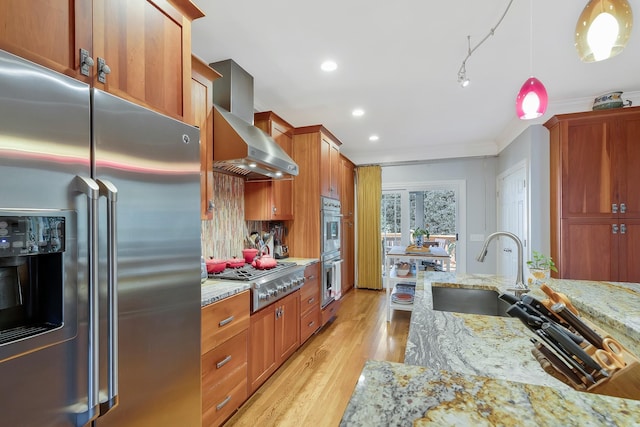 kitchen featuring light wood-style floors, wall chimney exhaust hood, light stone countertops, a sink, and stainless steel appliances
