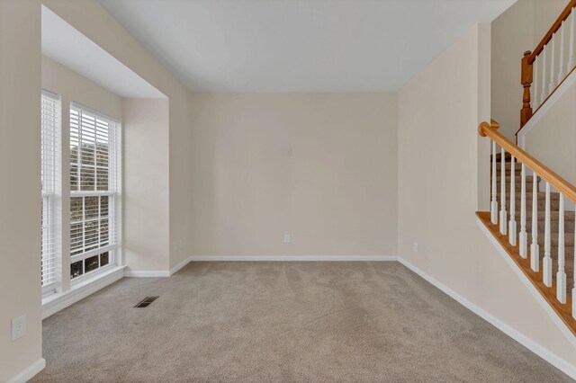 carpeted spare room featuring baseboards, visible vents, and stairs