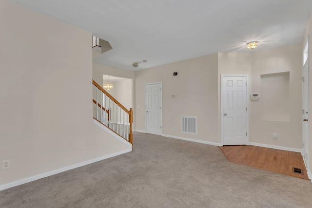 carpeted spare room featuring visible vents, baseboards, stairway, and a notable chandelier