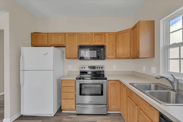 kitchen with light countertops, light wood finished floors, a sink, and black appliances