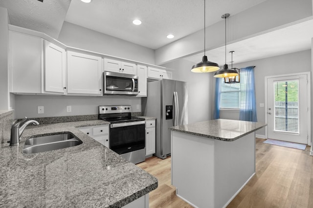 kitchen featuring light wood-style flooring, stainless steel appliances, white cabinets, a sink, and a center island