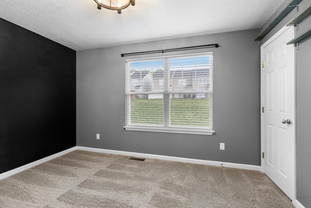 carpeted spare room featuring a textured ceiling, visible vents, and baseboards