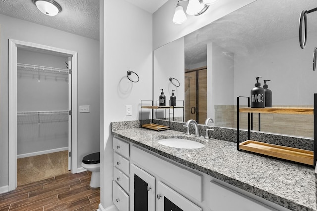 full bathroom with vanity, toilet, a stall shower, wood finish floors, and a textured ceiling