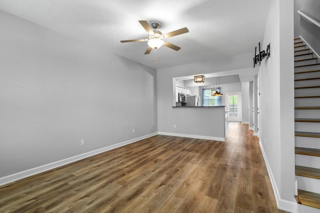 unfurnished living room with baseboards, ceiling fan, stairs, and dark wood-type flooring