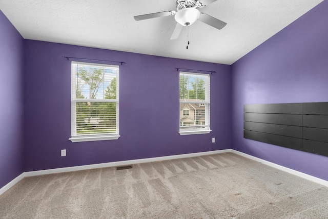 carpeted empty room with visible vents, a ceiling fan, vaulted ceiling, and baseboards
