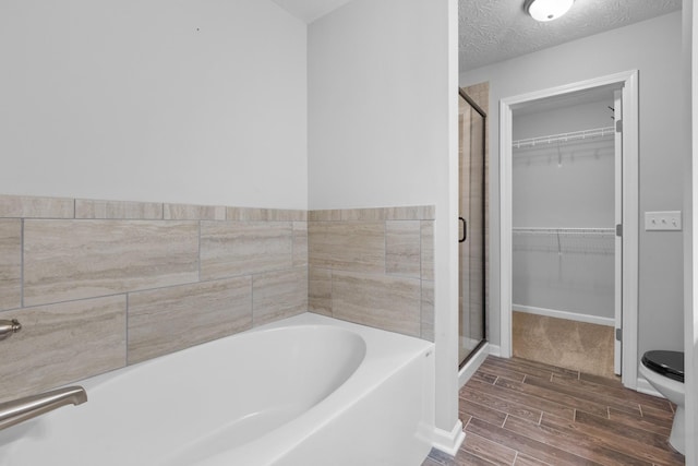 full bathroom featuring a shower stall, toilet, a bath, wood finished floors, and a spacious closet