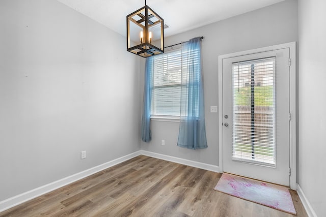 doorway featuring baseboards, wood finished floors, and an inviting chandelier