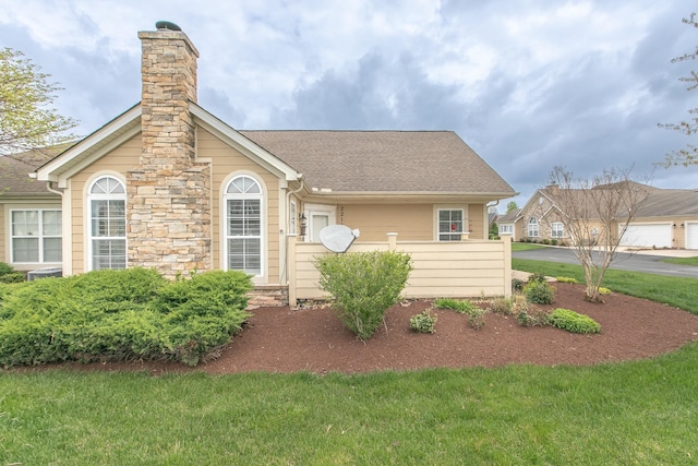 view of front of home with a front yard, a shingled roof, and a chimney