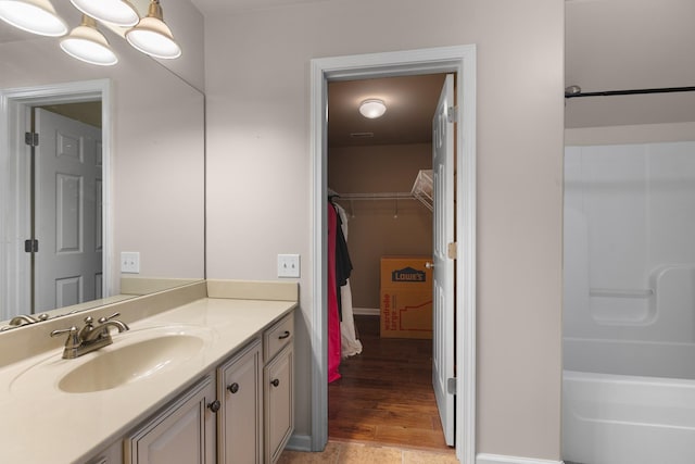 full bathroom featuring a walk in closet, vanity, baseboards, and wood finished floors