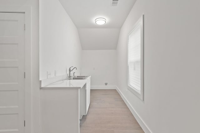 clothes washing area featuring baseboards, light wood finished floors, a sink, and visible vents