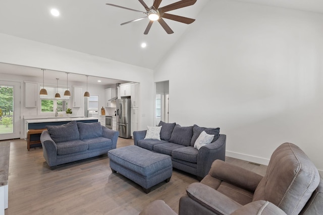 living room with baseboards, ceiling fan, light wood-type flooring, recessed lighting, and high vaulted ceiling