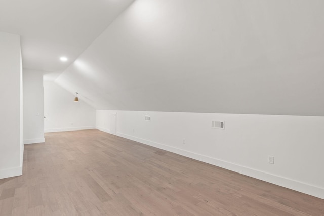 bonus room featuring light wood finished floors, visible vents, baseboards, and vaulted ceiling