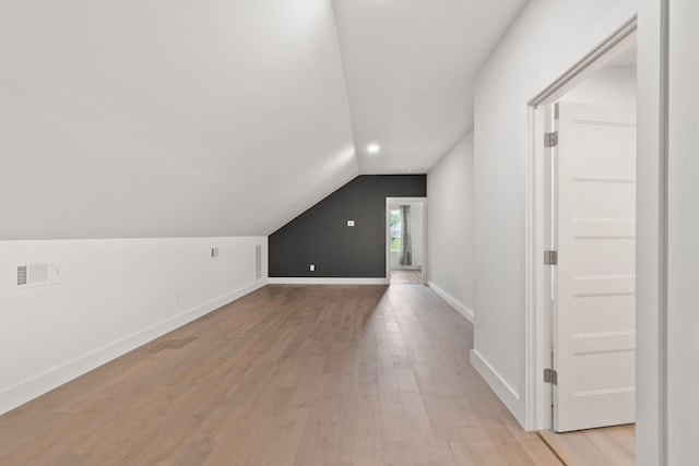 additional living space with light wood-style flooring, visible vents, baseboards, and vaulted ceiling