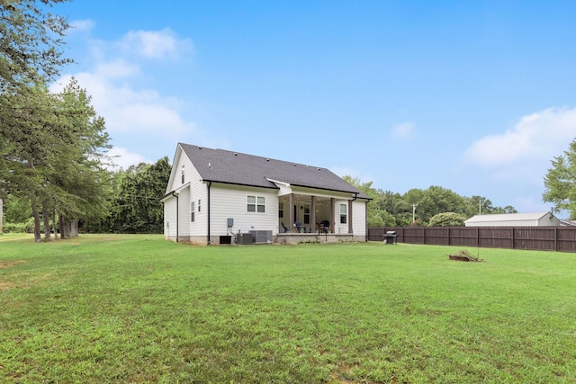 back of property with a shingled roof, cooling unit, fence, and a lawn