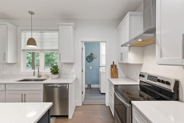 kitchen featuring wall chimney exhaust hood, washer / clothes dryer, white cabinets, a sink, and stainless steel appliances