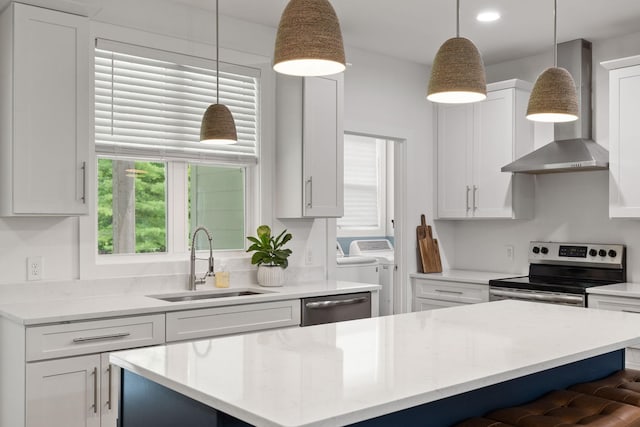 kitchen with wall chimney range hood, white cabinetry, appliances with stainless steel finishes, a sink, and washer and dryer