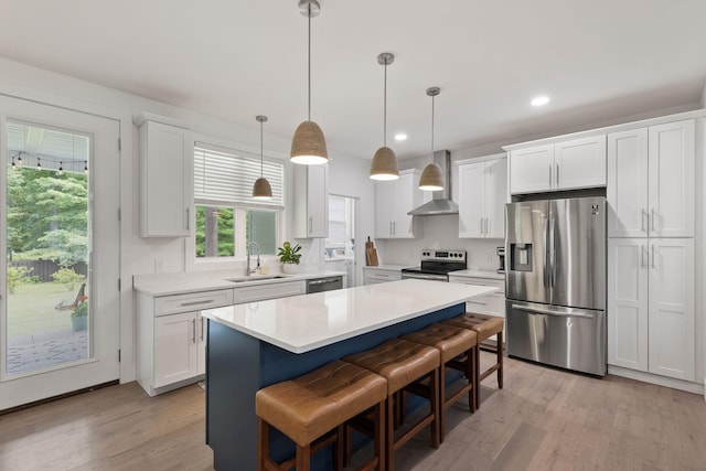 kitchen with light countertops, light wood-style floors, wall chimney exhaust hood, stainless steel appliances, and a sink