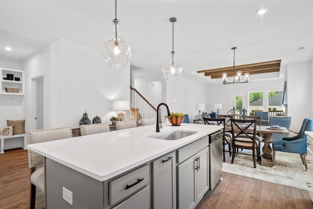 kitchen featuring stainless steel dishwasher, wood finished floors, a sink, open floor plan, and light countertops