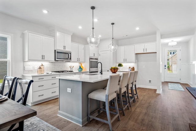 kitchen with white cabinets, light countertops, wood finished floors, stainless steel microwave, and decorative backsplash